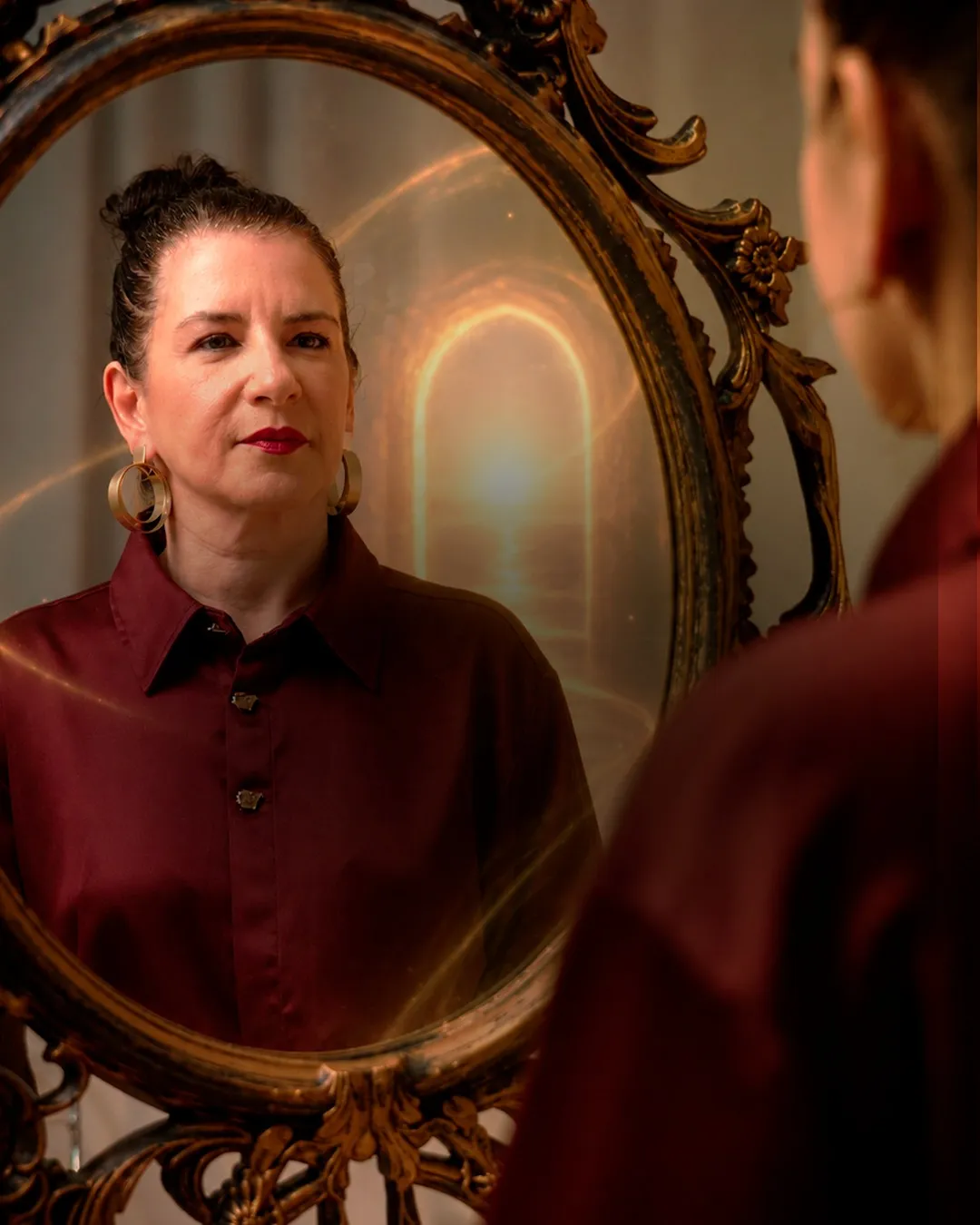 Paty Geaabra diante de um espelho dourado, com um portal de luz refletido atrás dela